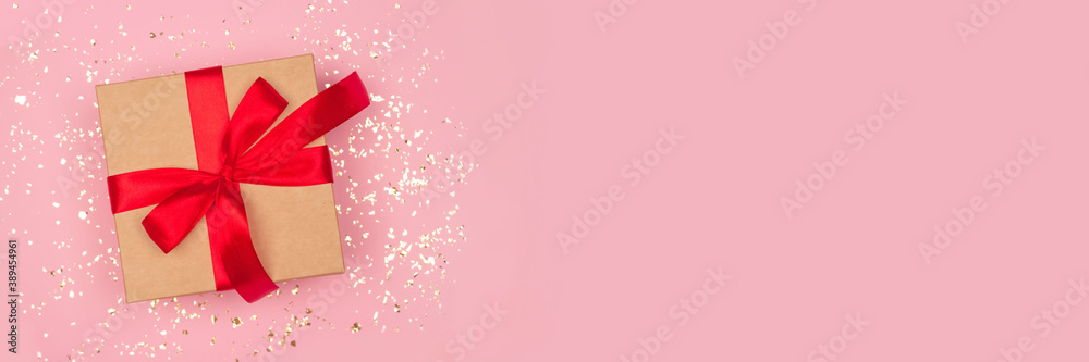 Festive banner - gift box with red bow on festive pink background with golden sparkles around and copyspace. Flat lay style. Christmas, New Year, Valentines Day and birthday celebration concept - obrazy, fototapety, plakaty 
