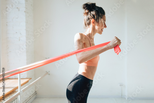 Fitness young woman working out using rubber band. Female athlete doing stretching exercises with resistance band
