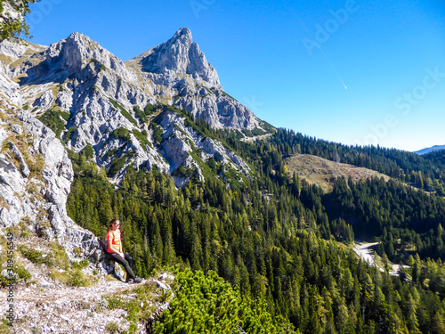 A woman hiking in a massive, stony mountains in Kaiserau Kreuzkogel region, Austrian Alps. She is enjoying the Alpine landscape. Many sharp peaks surrounding her. Sunny summer day
