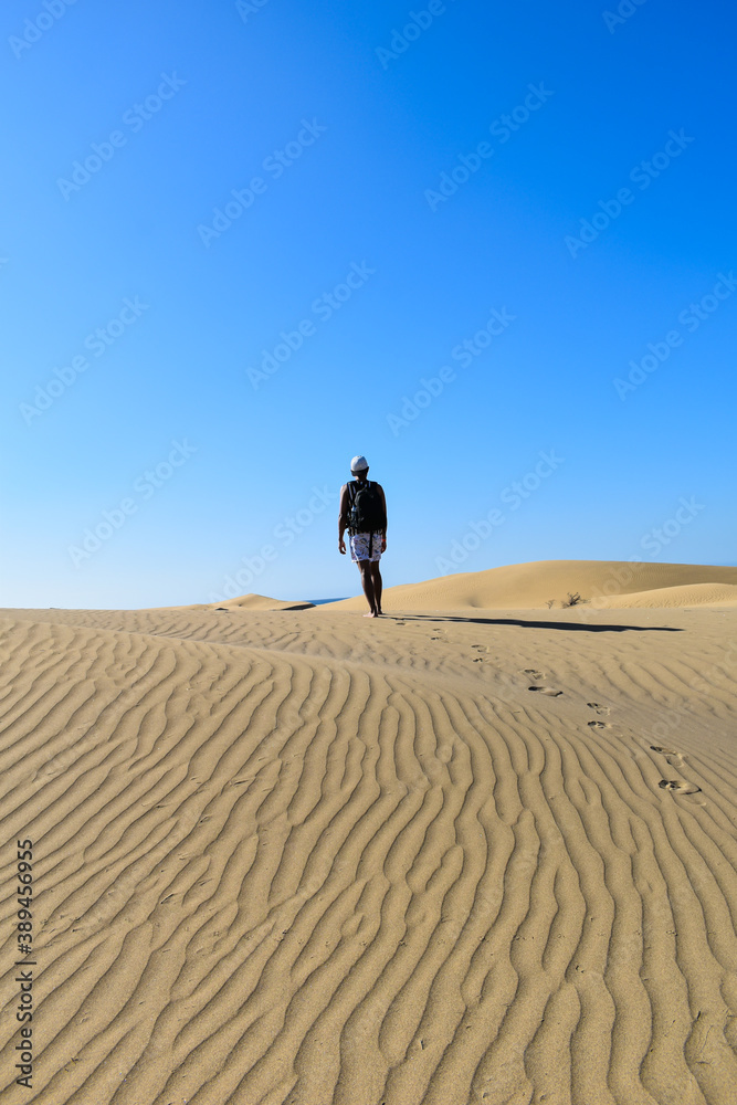 Lonely traveler walking through desert sand dunes with backpack.