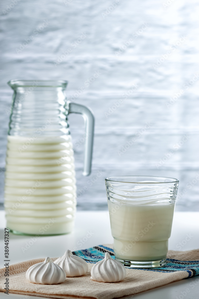 Natural whole milk in a jug and glass with bizet on a white brick wall background Natural whole milk in a jug and glass with bizet on a white brick wall background