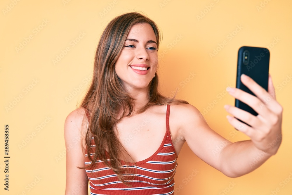 Beautiful young caucasian woman taking a selfie photo with smartphone looking positive and happy standing and smiling with a confident smile showing teeth Beautiful young caucasian woman taking a selfie photo with smartphone looking positive and happy standing and smiling with a confident smile showing teeth