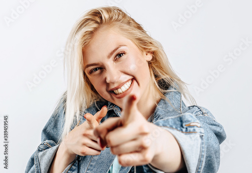 Beautiful young girl fooling around and pointing fingers at screen on gray isolated background