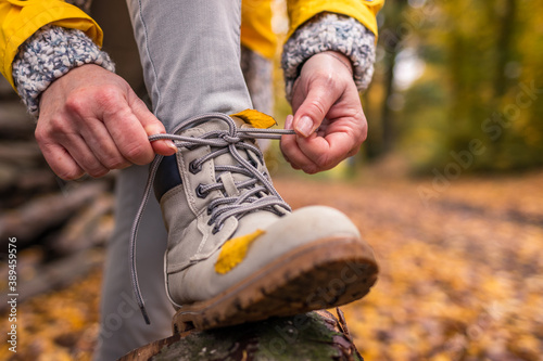 Woman tying shoelace on her hiking boot. Tourist is getting ready for autumn hike in forest