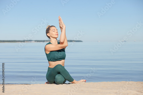 Woman in green sportswear practices yoga by sea © zhagunov_a