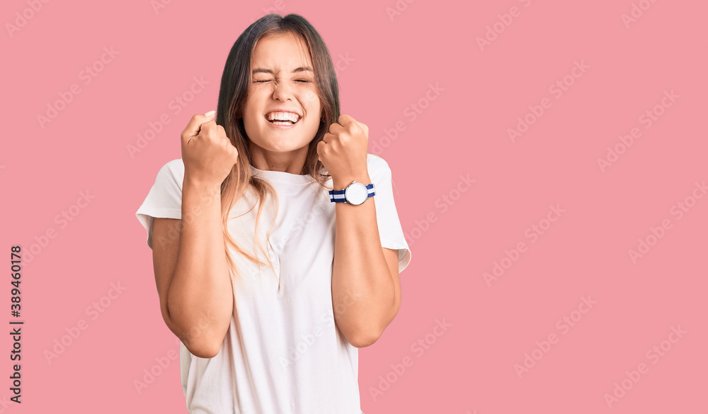 Beautiful caucasian woman wearing casual white tshirt excited for success with arms raised and eyes closed celebrating victory smiling. winner concept. Beautiful caucasian woman wearing casual white tshirt excited for success with arms raised and eyes closed celebrating victory smiling. winner concept.