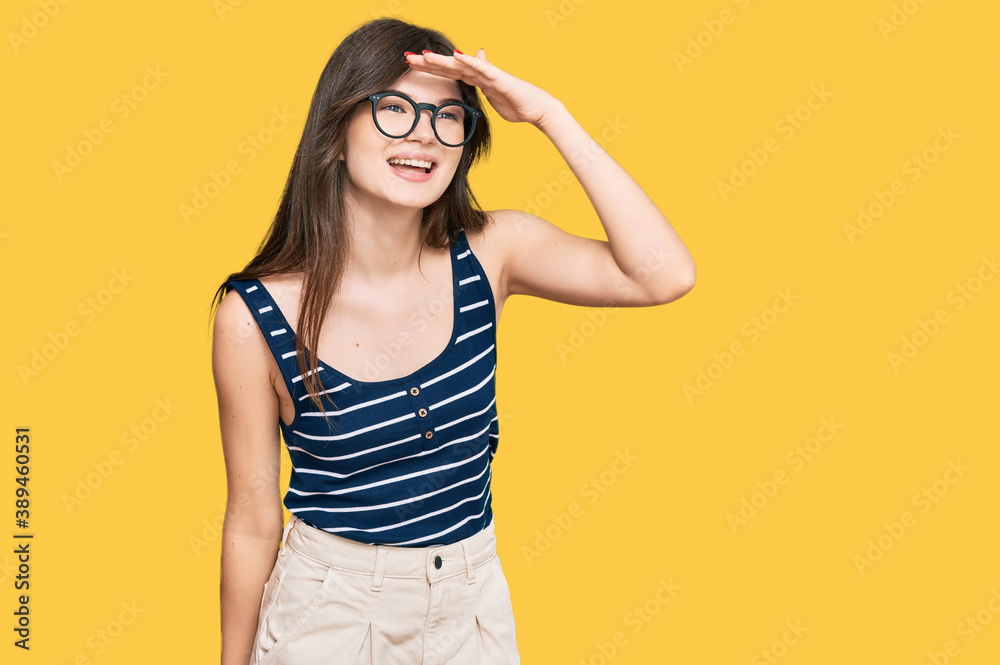 Young beautiful caucasian girl wearing casual clothes and glasses very happy and smiling looking far away with hand over head. searching concept.