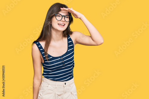 Young beautiful caucasian girl wearing casual clothes and glasses very happy and smiling looking far away with hand over head. searching concept. © Krakenimages.com