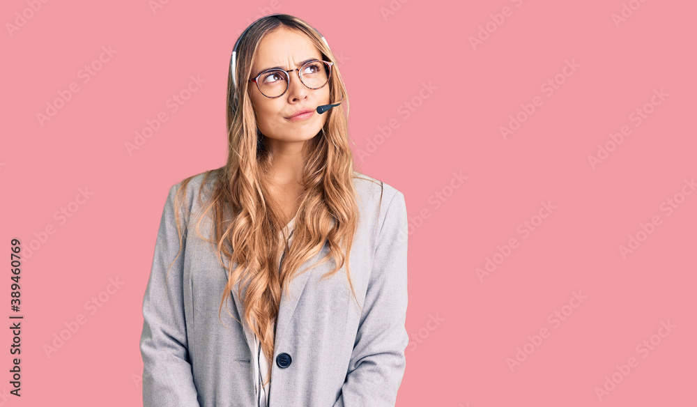 Young beautiful blonde woman wearing call center agent headset smiling looking to the side and staring away thinking.