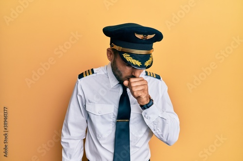 Фотография Handsome hispanic man wearing airplane pilot uniform feeling unwell and coughing as symptom for cold or bronchitis