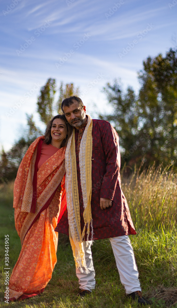Mid aged couple wearing traditional Indian clouds on lit by the sunset meadow