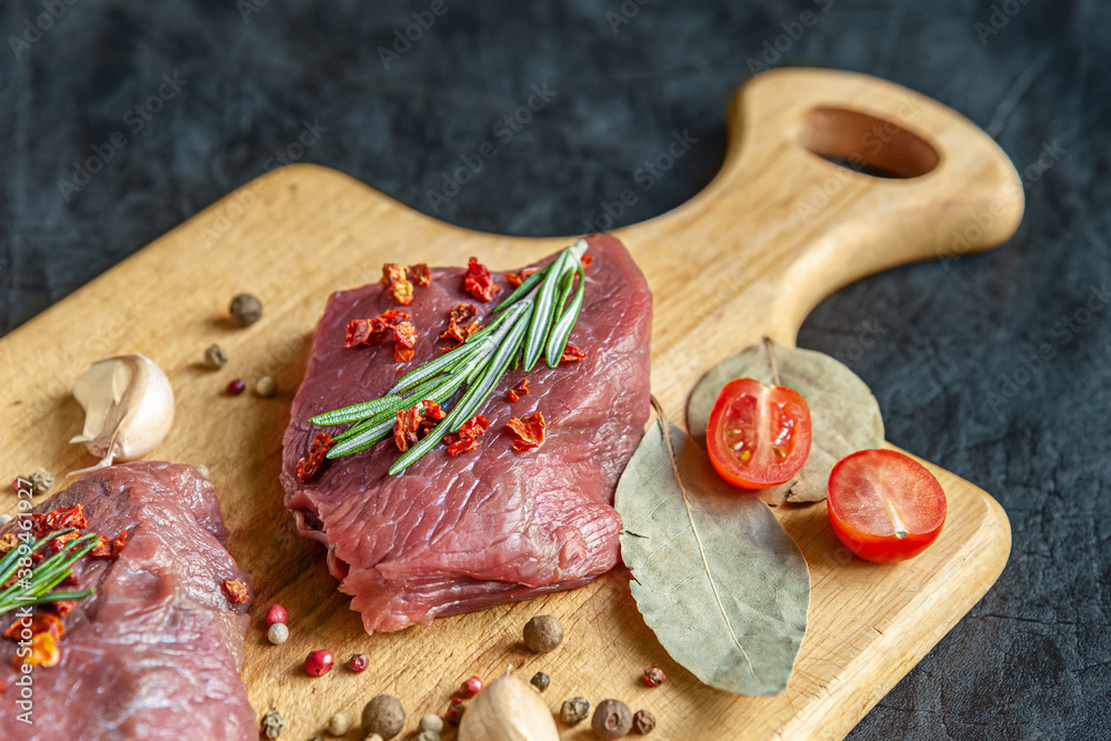 raw meat with spices, cherry tomatoes and garlic on a wooden cutting board close up