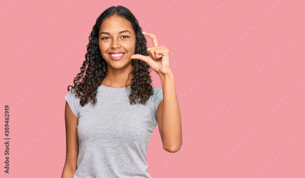 Young african american girl wearing casual clothes smiling and confident gesturing with hand doing small size sign with fingers looking and the camera. measure concept. Young african american girl wearing casual clothes smiling and confident gesturing with hand doing small size sign with fingers looking and the camera. measure concept.