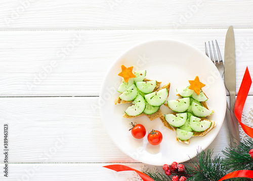 Creative idea for decorating New Year's snacks. Vegetarian and dietary concept. Sandwiches in the form of a Christmas tree with a cucumber and a carrot,tomatoes on a plate on a white wooden background