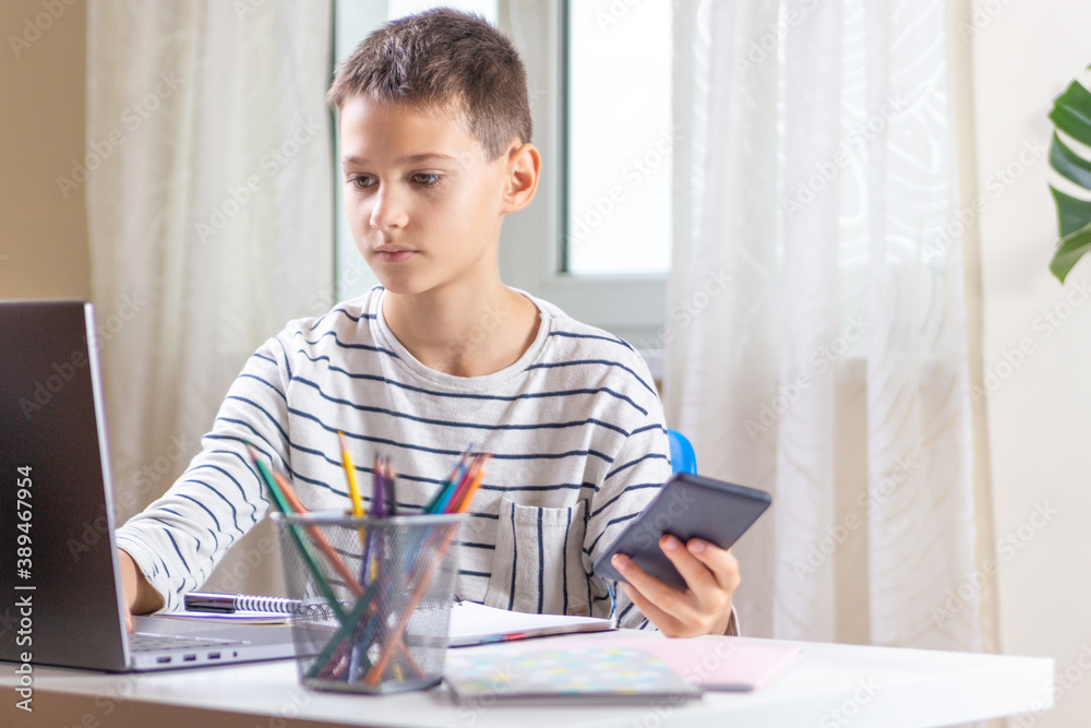 Kid sitting with laptop computer and scrolling phone instead of doing homework. Technology, online learning, entertainment at home Kid sitting with laptop computer and scrolling phone instead of doing homework. Technology, online learning, entertainment at home