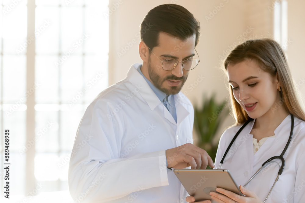 Teamwork and brainstorming. Two doctors colleagues millennial male and female working with history case of clinic customer on digital tablet, studying lab tests results or using diagnostic medical app