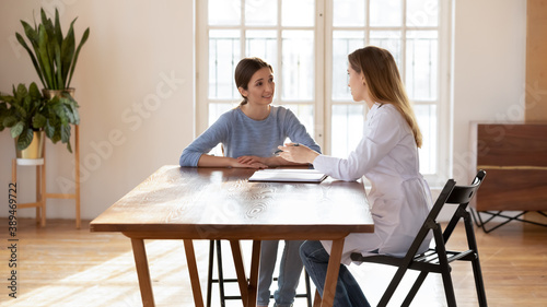 Attentive woman patient sitting at desk at doctor office listening to recommendations of female GP or counsel of psychologist, medical advisor proposing regular insurance policy to interested customer