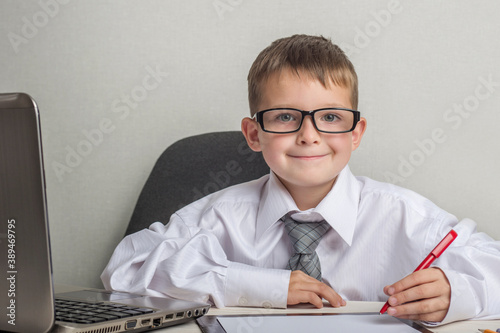 An adorable child is writing on a clipboard in suit and glasses. Little boss in the office. Children pretend to be adults