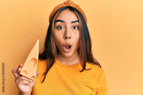 Young latin woman eating emmental cheese scared and amazed with open mouth for surprise, disbelief face
