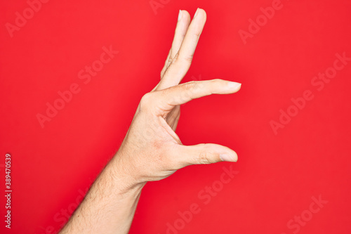 Hand of caucasian young man showing fingers over isolated red background picking and taking invisible thing  holding object with fingers showing space