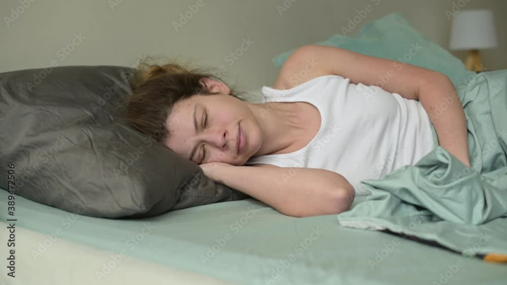 A young woman is woken up in the morning and annoyed by noise from neighbors or from the street. The woman gets angry and covers herself with a second pillow to drown out the annoying noise A young woman is woken up in the morning and annoyed by noise from neighbors or from the street. The woman gets angry and covers herself with a second pillow to drown out the annoying noise