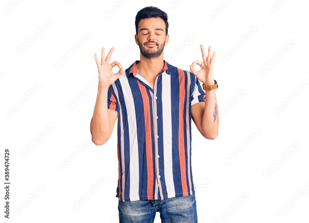 Young handsome hispanic man wearing casual summer shirt relax and smiling with eyes closed doing meditation gesture with fingers. yoga concept. Young handsome hispanic man wearing casual summer shirt relax and smiling with eyes closed doing meditation gesture with fingers. yoga concept.