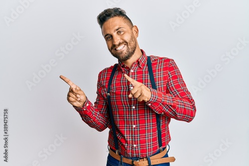 Handsome man with beard wearing hipster elegant look smiling and looking at the camera pointing with two hands and fingers to the side.