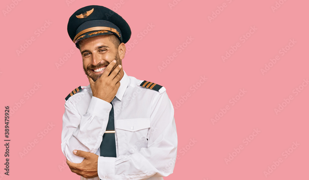 Handsome man with beard wearing airplane pilot uniform looking confident at the camera smiling with crossed arms and hand raised on chin. thinking positive. Handsome man with beard wearing airplane pilot uniform looking confident at the camera smiling with crossed arms and hand raised on chin. thinking positive.