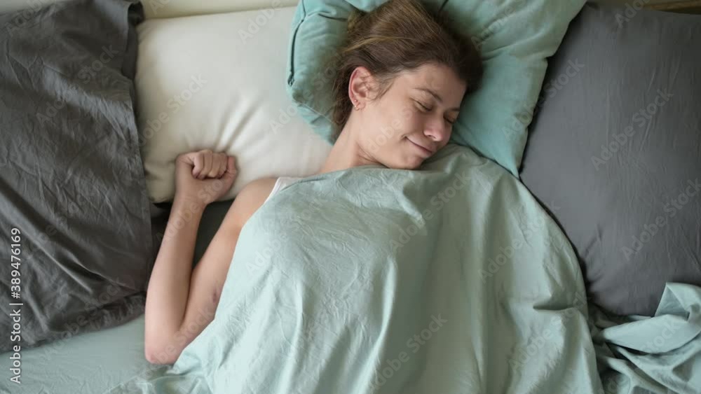 A young woman is basking in bed in the morning on a day off. She does not need to rush anywhere, because today she is resting and can sleep