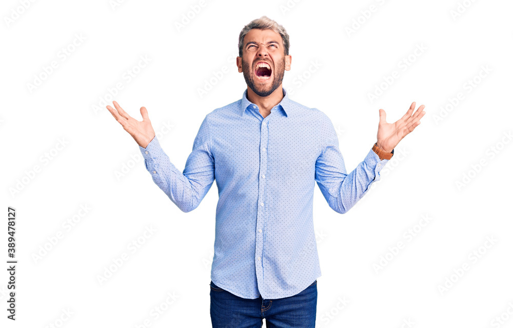 Young handsome blond man wearing elegant shirt crazy and mad shouting and yelling with aggressive expression and arms raised. frustration concept. Young handsome blond man wearing elegant shirt crazy and mad shouting and yelling with aggressive expression and arms raised. frustration concept.