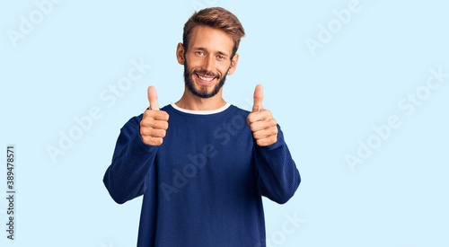 Handsome blond man with beard wearing casual sweater success sign doing positive gesture with hand, thumbs up smiling and happy. cheerful expression and winner gesture.