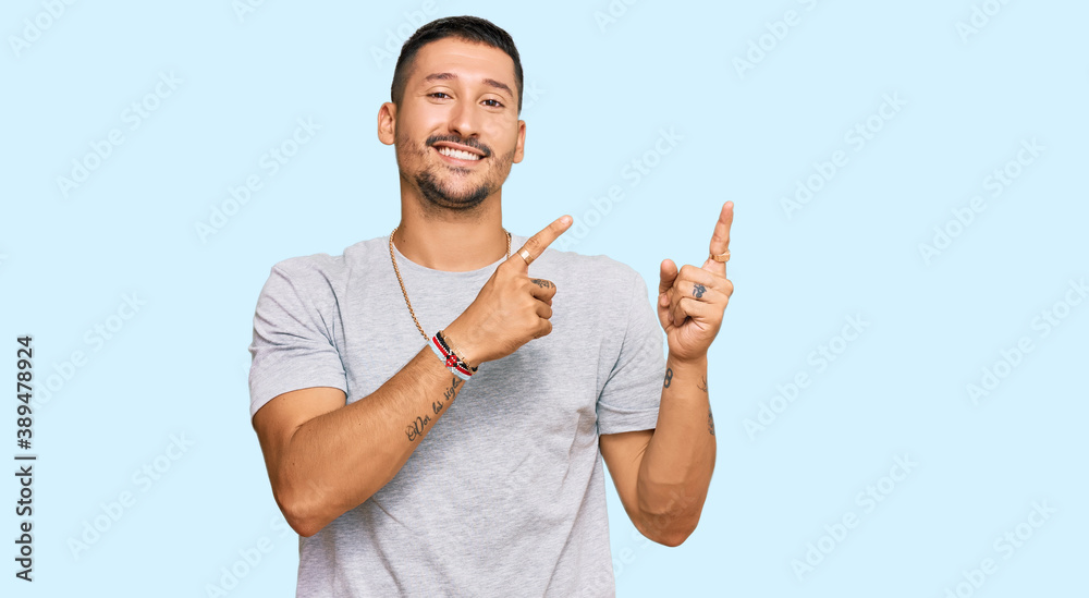 Handsome man with tattoos wearing 90s style smiling and looking at the camera pointing with two hands and fingers to the side. Handsome man with tattoos wearing 90s style smiling and looking at the camera pointing with two hands and fingers to the side.
