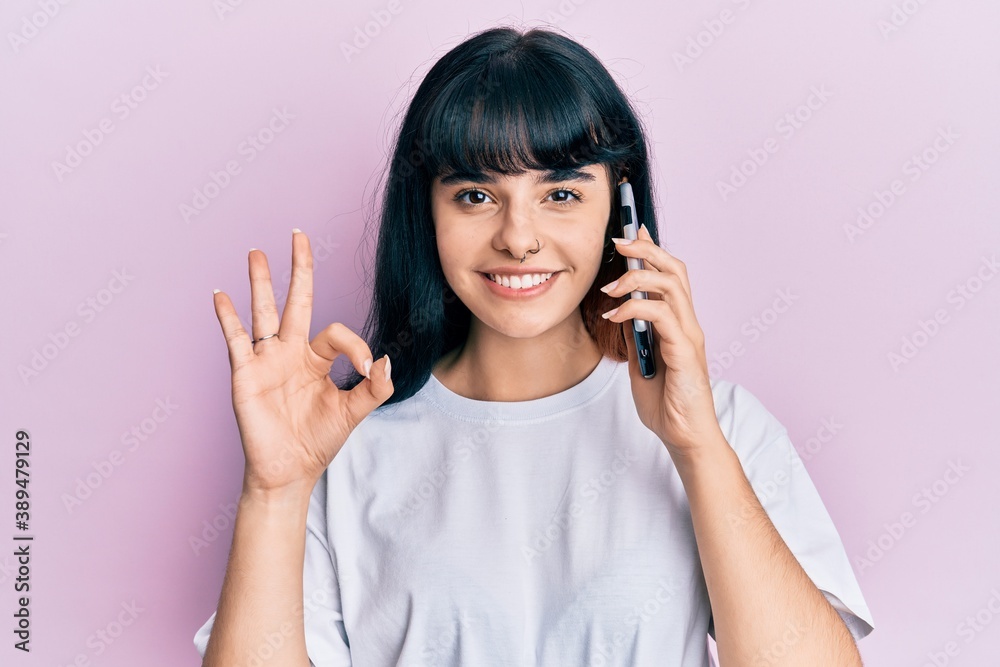 Young hispanic girl having conversation talking on the smartphone doing ok sign with fingers, smiling friendly gesturing excellent symbol Young hispanic girl having conversation talking on the smartphone doing ok sign with fingers, smiling friendly gesturing excellent symbol