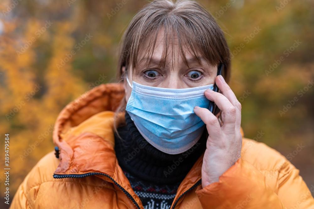 A woman in a medical mask walks in the autumn park. The woman is very emotionally talking on the phone. A woman in a medical mask walks in the autumn park. The woman is very emotionally talking on the phone.