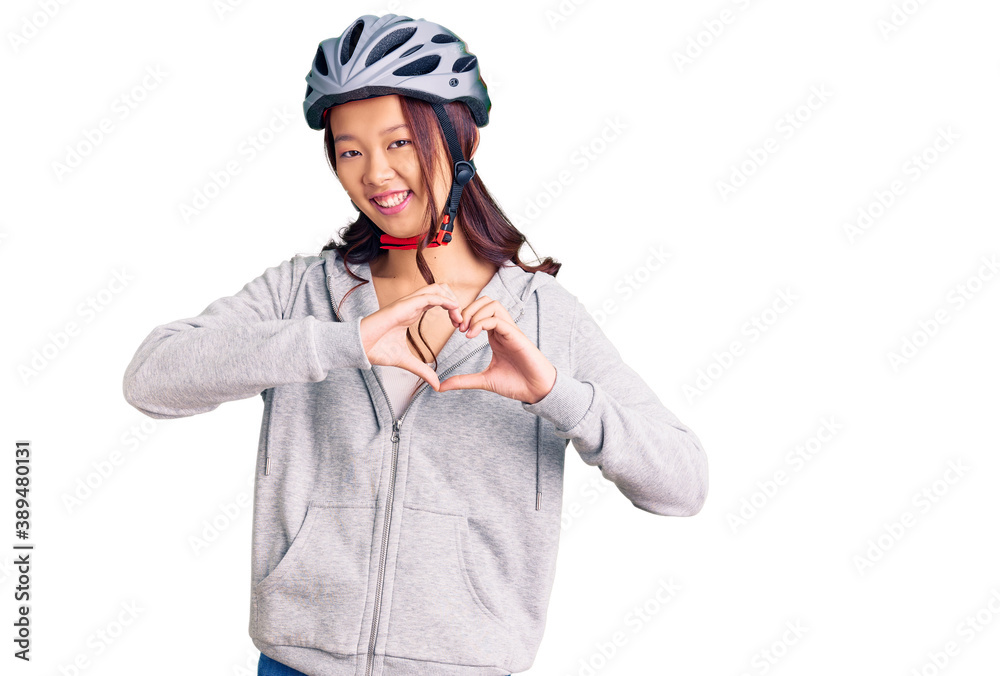 Young beautiful chinese girl wearing bike helmet smiling in love showing heart symbol and shape with hands. romantic concept. Young beautiful chinese girl wearing bike helmet smiling in love showing heart symbol and shape with hands. romantic concept.