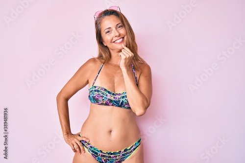 Middle age hispanic woman wearing bikini looking confident at the camera with smile with crossed arms and hand raised on chin. thinking positive.