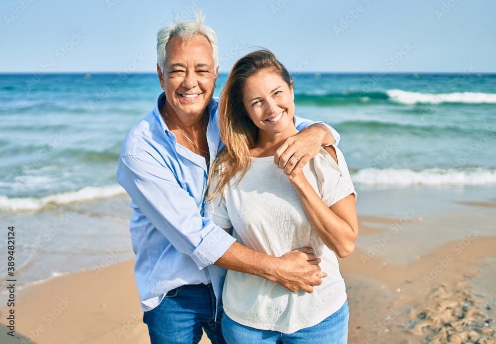 Middle age hispanic couple smiling happy and hugging walking at the beach Middle age hispanic couple smiling happy and hugging walking at the beach