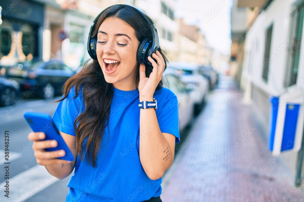 Young hispanic woman smiling happy using smartphone and headphones at the city. Young hispanic woman smiling happy using smartphone and headphones at the city.