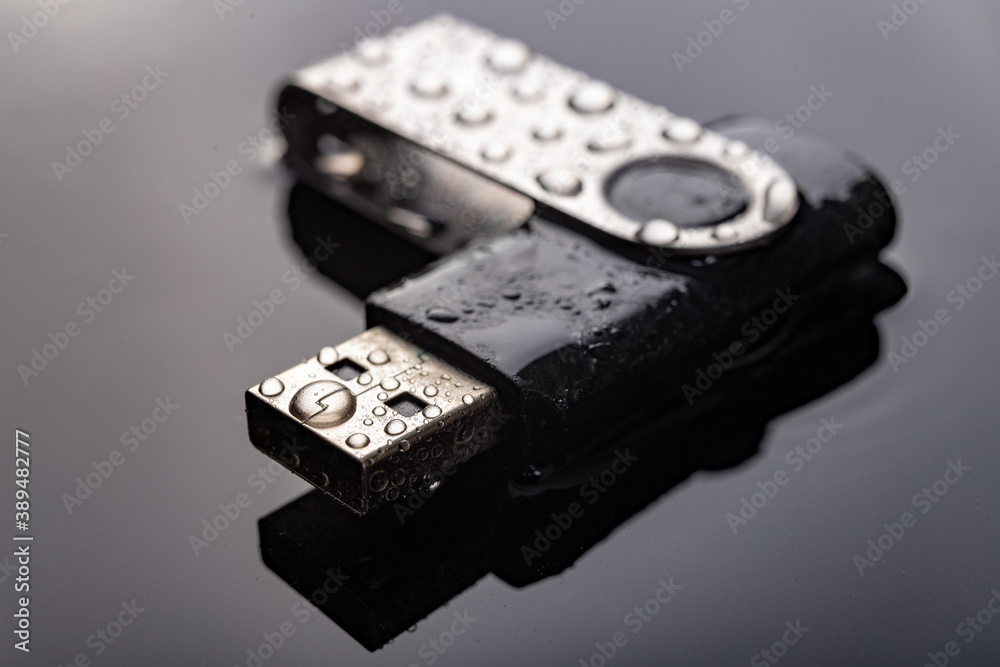 USB flash drive with water drops on the table. Electronic data storage device poured over with water.