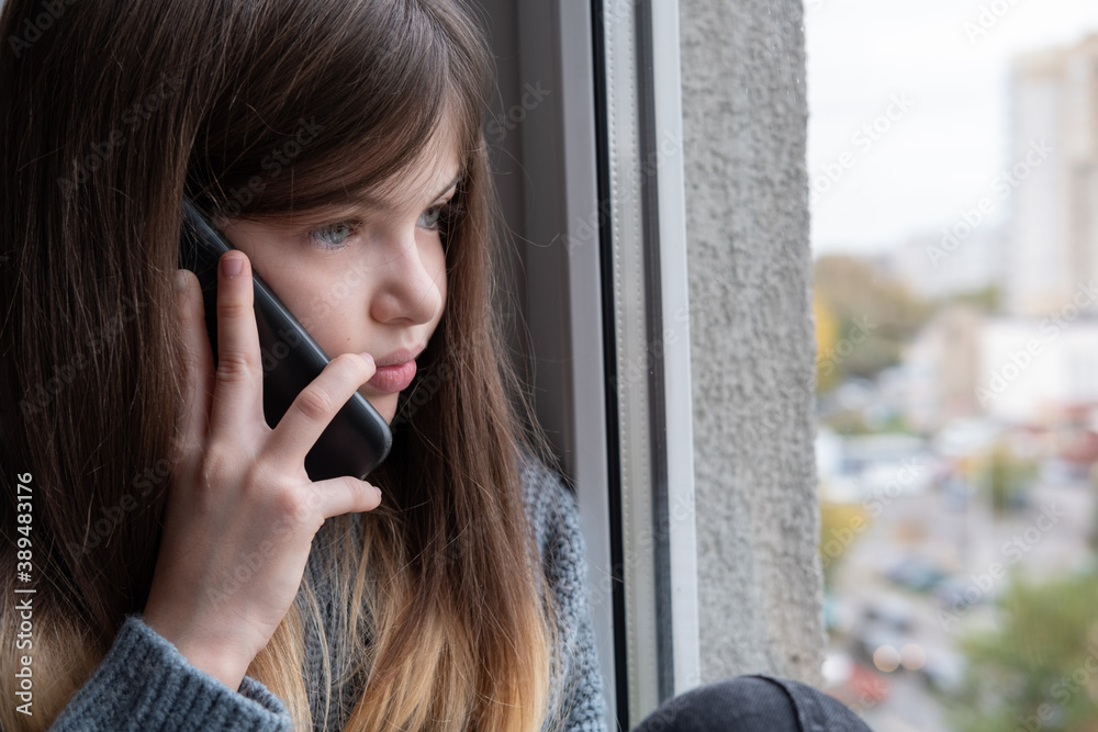 Little / young girl sitting by the window and talking on the phone