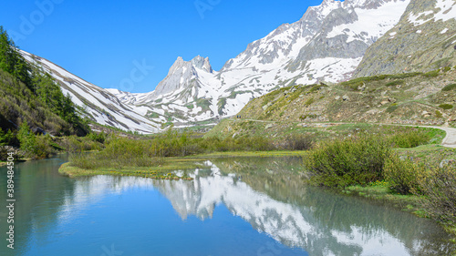 Fototapeta Naklejka Na Ścianę i Meble -  Mountains peaks mirroring in the lake showing symmetry. Mountains are full of snow and the water is calm. Val Veny, Italy