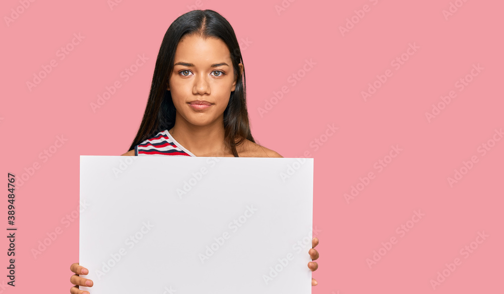 Beautiful hispanic woman holding blank empty banner thinking attitude and sober expression looking self confident Beautiful hispanic woman holding blank empty banner thinking attitude and sober expression looking self confident