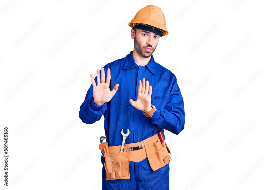 Young hispanic man wearing worker uniform moving away hands palms showing refusal and denial with afraid and disgusting expression. stop and forbidden. Young hispanic man wearing worker uniform moving away hands palms showing refusal and denial with afraid and disgusting expression. stop and forbidden.