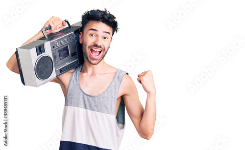 Young hispanic man holding boombox, listening to music screaming proud, celebrating victory and success very excited with raised arms