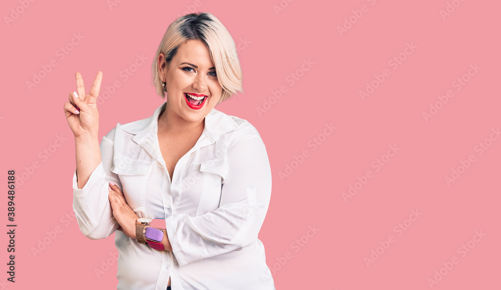 Young blonde plus size woman wearing casual shirt smiling with happy face winking at the camera doing victory sign. number two. Young blonde plus size woman wearing casual shirt smiling with happy face winking at the camera doing victory sign. number two.