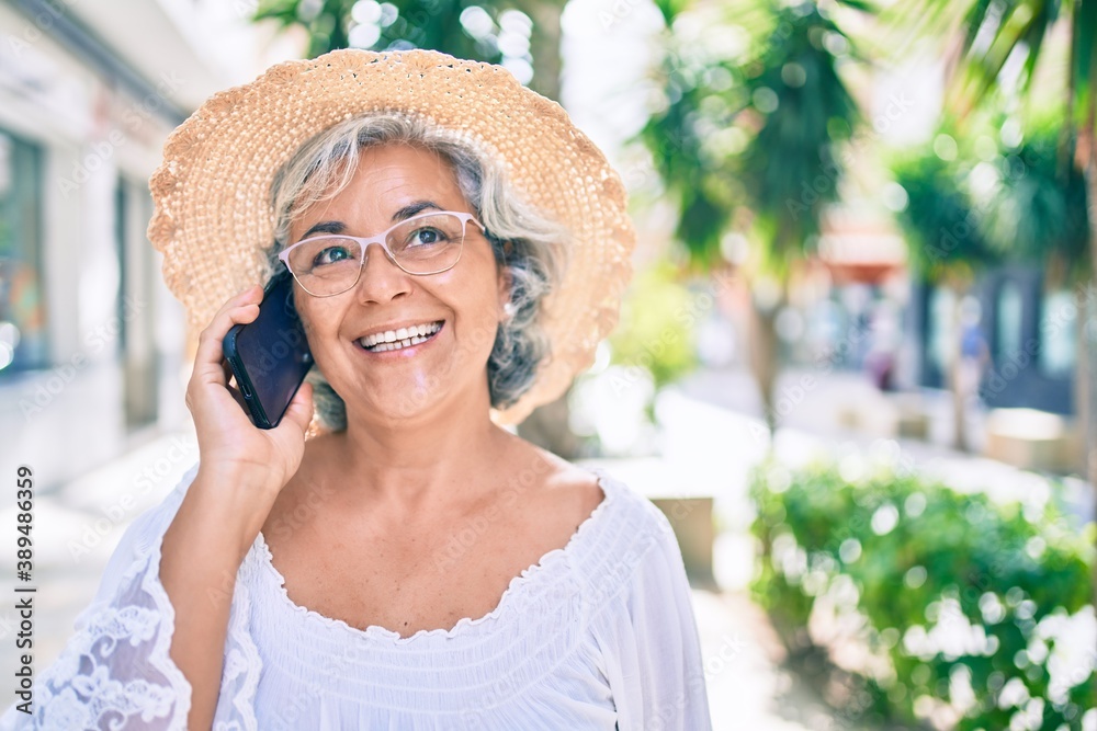 Middle age woman with grey hair smiling happy outdoors speaking on the phone