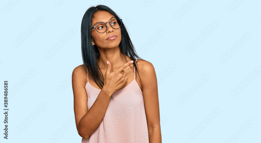 Fototapeta premium Young african american woman wearing casual clothes and glasses pointing with hand finger to the side showing advertisement, serious and calm face