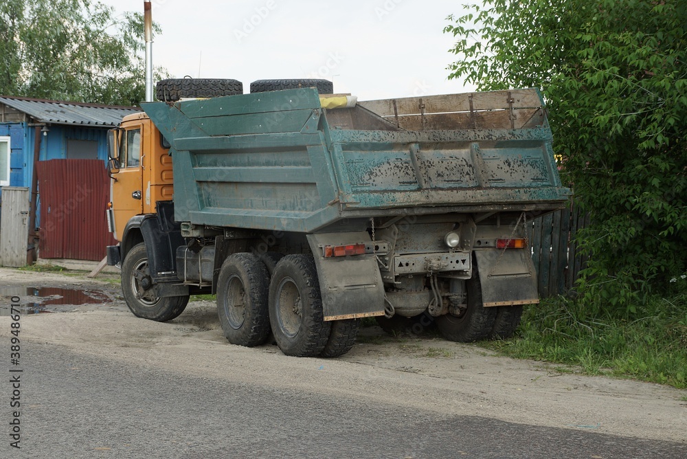 one big old green dump truck stands on a gray asphalt road on the street near the fence