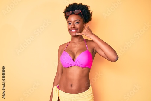 Young african american woman wearing bikini smiling doing phone gesture with hand and fingers like talking on the telephone. communicating concepts.