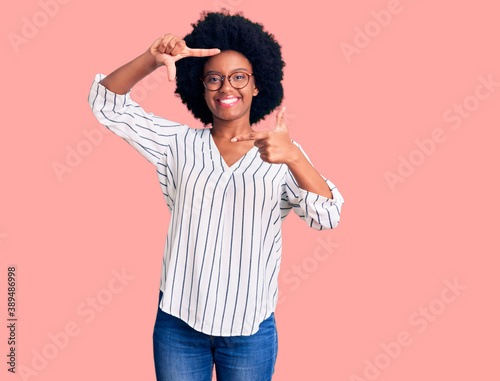 Young african american woman wearing casual clothes and glasses smiling making frame with hands and fingers with happy face. creativity and photography concept.